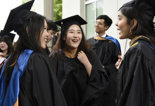 Three recently graduated Goizueta Alumni pose in cap and gowns after commencement