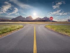 Crossing with stop sign towards the sun and mountain peaks with yellow line on asphalt. Success and vision concept.