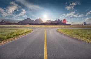 Crossing with stop sign towards the sun and mountain peaks with yellow line on asphalt. Success and vision concept.