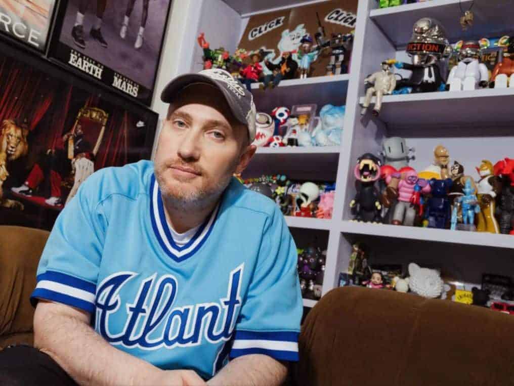 Josh Luber 99BBA 06JD/MBA poses at his home in front of a shelf of collectibles, including many from his new company, ghostwrite.