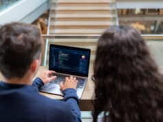 Two software developers working together on coding and system management on a laptop. Professional programmers collaborating on web development and software engineering in a modern tech office workspace.