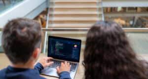 Two software developers working together on coding and system management on a laptop. Professional programmers collaborating on web development and software engineering in a modern tech office workspace.
