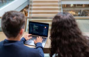 Two software developers working together on coding and system management on a laptop. Professional programmers collaborating on web development and software engineering in a modern tech office workspace.