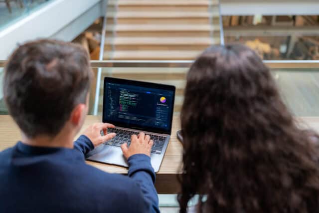 Two software developers working together on coding and system management on a laptop. Professional programmers collaborating on web development and software engineering in a modern tech office workspace.
