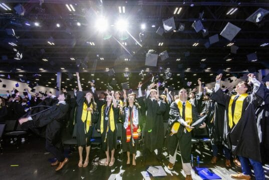 Goizueta Business School graduates celebrate by tossing their caps in the air during the Class of 2026 commencement ceremony at Gas South Arena.