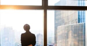 Professional standing by a window overlooking a city skyline.