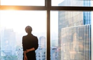 Faculty Perspective: The Leadership Transition No One Prepares You For Professional standing by a window overlooking a city skyline.