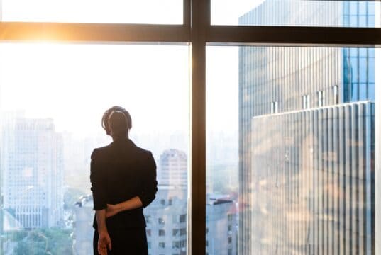 Professional standing by a window overlooking a city skyline.