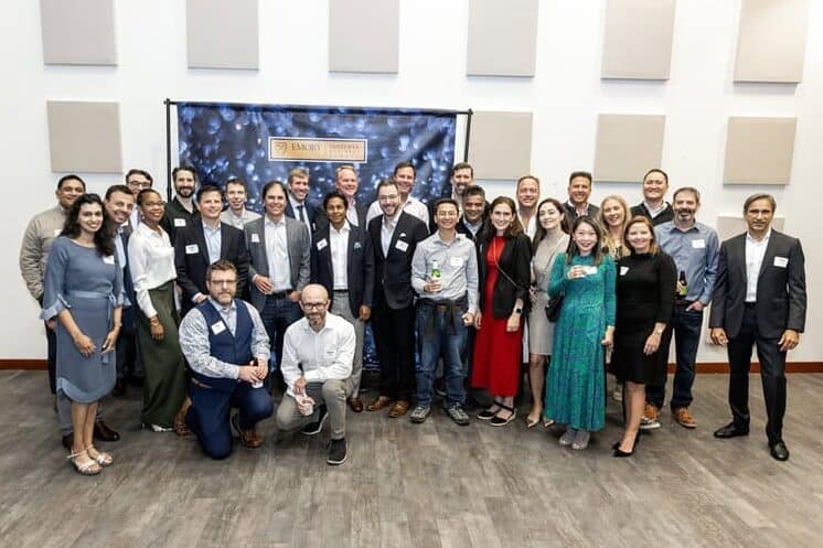 A large group of MBA alumni pose together at an indoor reunion celebration in front of an Emory Goizueta backdrop.
